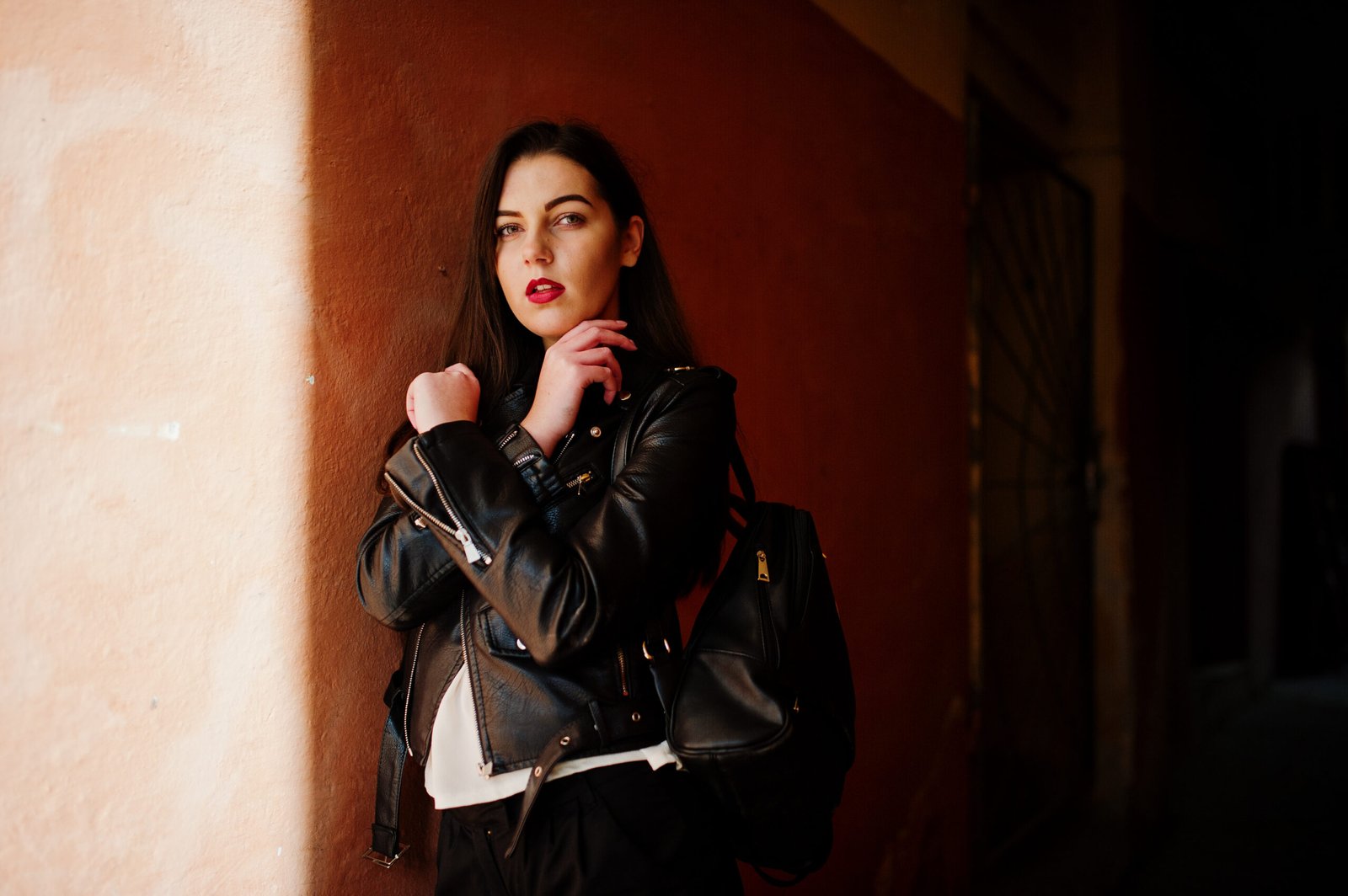 Stylish Brunette Girl Wear Leather Jacket Shorts With Backpack Against Orange Wall Shadows Scaled